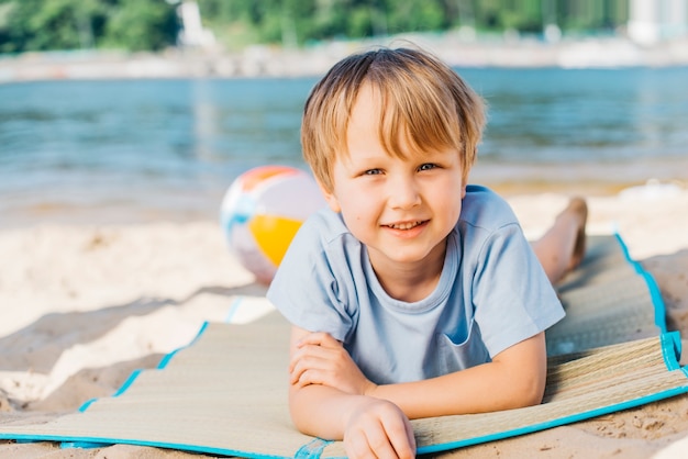 Kleiner Junge, der Kamera betrachtet und auf Strand lächelt