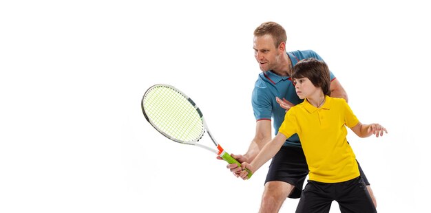 Kleiner Junge, der lernt, wie man Tennis spielt, mit einem professionellen Sportlehrer, der über weißem Studiohintergrund isoliert ist