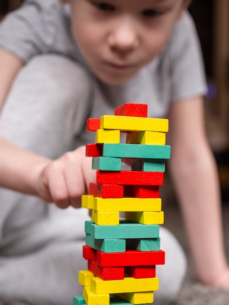 Kostenloses Foto kleiner junge, der mit buntem holzturmspiel überzieht