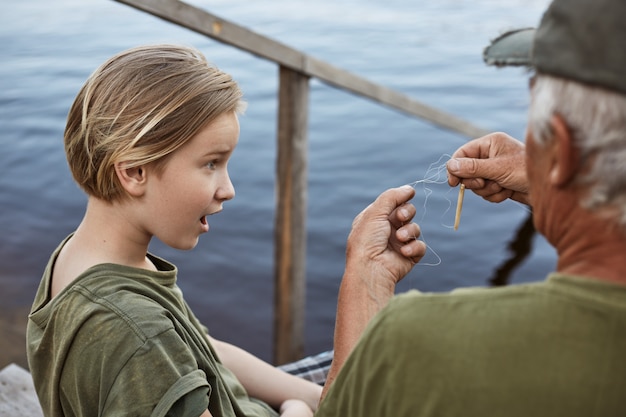 Kleiner Junge, der mit seinem Vater fischt, erstaunt wegen der verwickelten Schnur an der Angelrute, Familie posiert auf Holztreppen, die zum Wasser führen, überrascht männliches Kind.