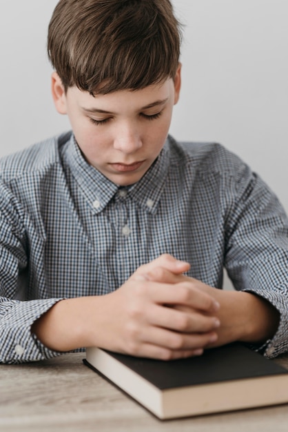 Kostenloses Foto kleiner junge, der mit seinen händen auf einer bibel betet