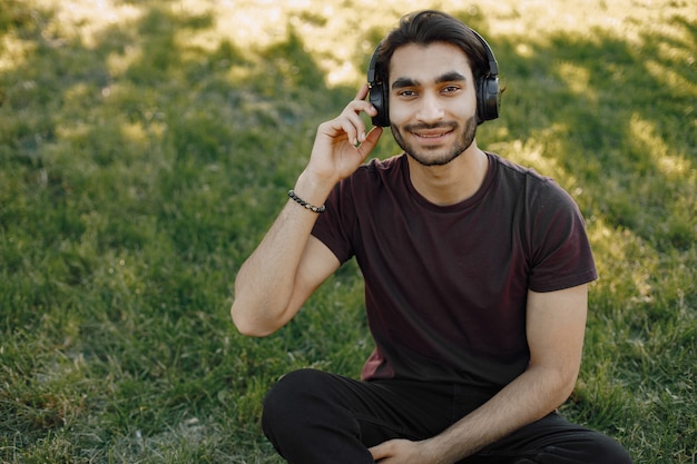 Kleiner Junge, der Musik hört, während er auf einem Gras sitzt. Mann hat einen großen Kopfhörer