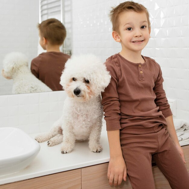 Kleiner Junge, der neben seinem Hund im Badezimmer sitzt