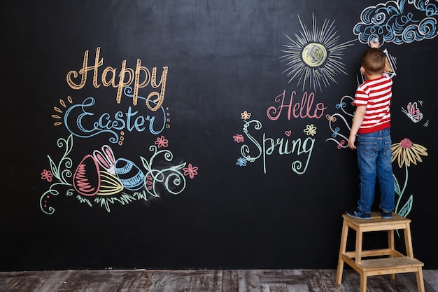 Kostenloses Foto kleiner junge, der ostern kritzeleien steht und zeichnet