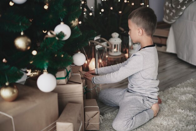 Kleiner Junge, der Weihnachtsgeschenke arrangiert