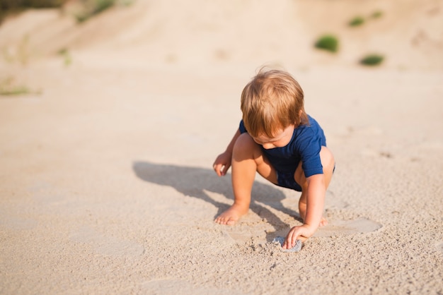 Kleiner Junge des hohen Winkels am Strand, der mit Sand spielt