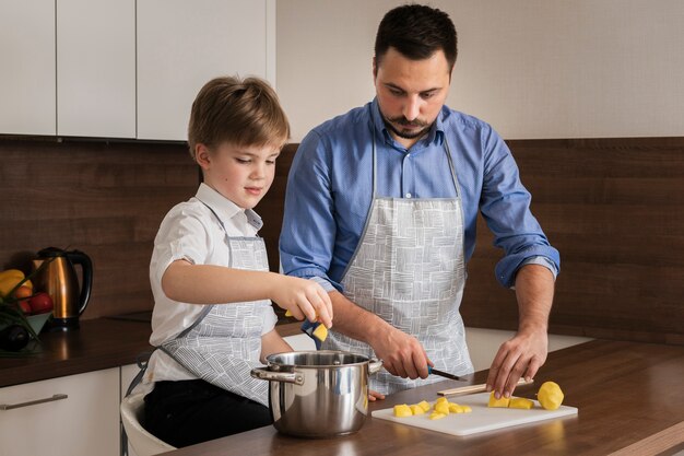 Kleiner Junge des hohen Winkels, der seinem Vati hilft zu kochen