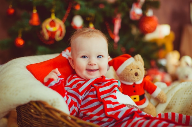 Kleiner Junge in abgestreiften Pyjamas sitzt vor einem Weihnachtsbaum