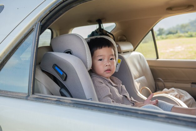 Kleiner Junge in einem Kindersitz, der geduldig auf der Rückseite eines Autos sitzt.