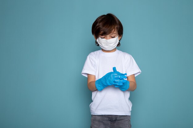 Kleiner Junge in weißer steriler Schutzmaske und blauen Handschuhen auf blauer Wand