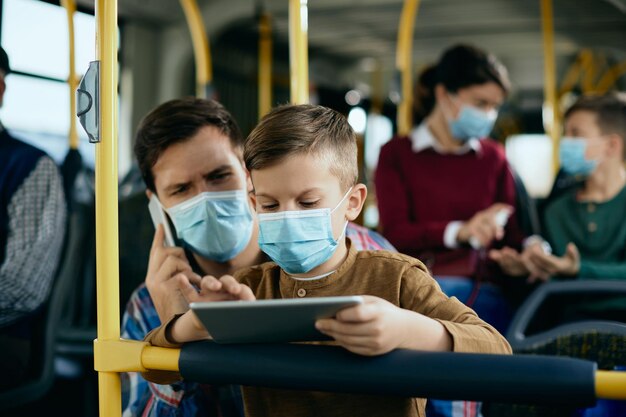 Kleiner Junge mit Gesichtsmaske mit digitalem Tablet, während er mit dem Bus fährt