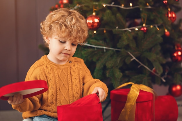 Kleiner Junge nahe Weihnachtsbaum in einer braunen Strickjacke