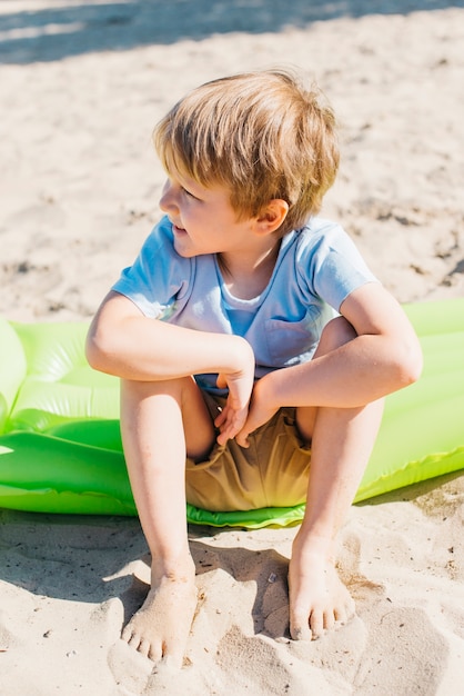 Kostenloses Foto kleiner junge sitzt auf sand