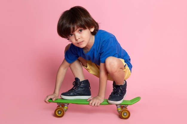 kleiner Kindjunge im blauen T-Shirt reitend auf Skateboard auf rosa Wand