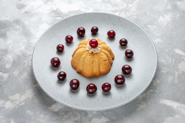 kleiner Kuchen in Teller mit Kirschen auf hellem Schreibtisch, Kuchenkeks süßer Zucker backen Obst