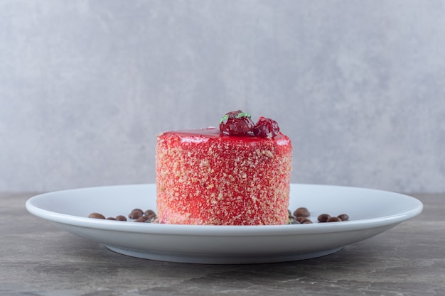 Kostenloses Foto kleiner kuchen, mit erdbeersirup-topping und kaffeebohnen auf einer platte auf marmoroberfläche