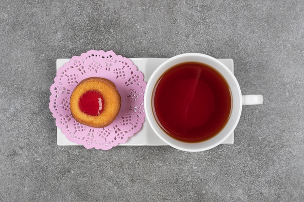 Kleiner Kuchen mit Gelee und Tasse Tee auf Marmoroberfläche