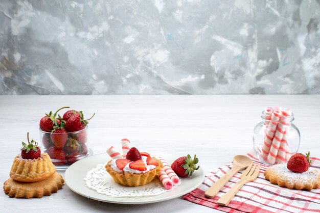 kleiner Kuchen mit Sahne und geschnittenen Erdbeerkuchen Bonbons auf weißem Schreibtisch, Obstkuchen Beerenzucker