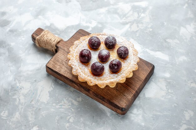 kleiner leckerer Kuchen mit Zuckerpulver und Kirschen auf hellem Schreibtisch, Obstkuchenkeks süß