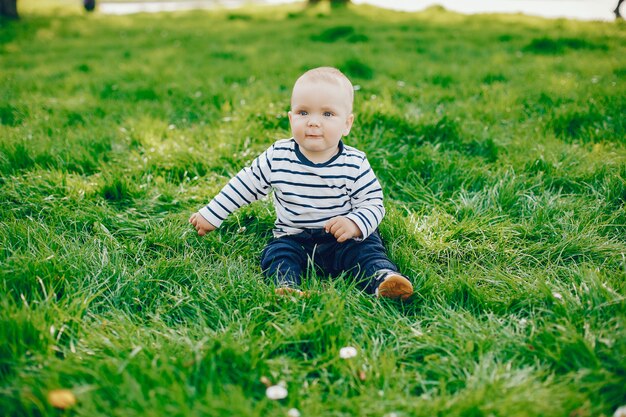 kleiner netter hübscher Junge sitzt auf einem grünen Gras in einem sonnigen Sommerpark