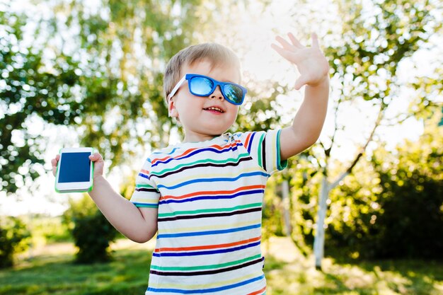 Kleiner süßer Junge gibt eine hohe Fünf und hält ein Telefon in der Hand.