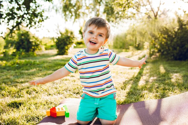 Kleiner süßer Junge sieht im Sommergarten mit seinem Spielzeughaus glücklich aus.