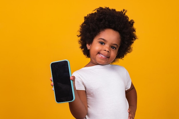 Kleines afrokindmädchen, das ein telefon hält und lokalisiert auf gelbem hintergrund zeigt.