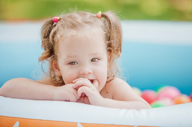 kleines Baby, das mit Spielzeug im aufblasbaren Pool im sonnigen Sommertag spielt