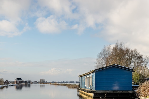 Kostenloses Foto kleines blaues haus über dem wasser mit gebäuden in der ferne unter einem blauen himmel