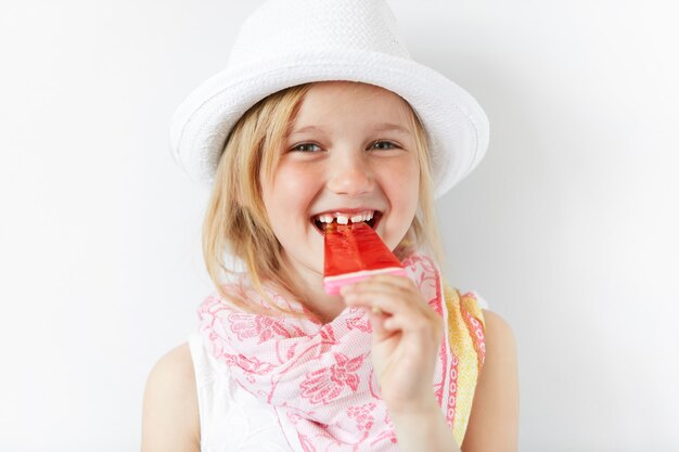 Kleines blondes Mädchen, das weißen Hut trägt und Eis isst