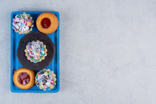 Kleines Dessertsortiment auf einer blauen Platte auf Marmortisch.