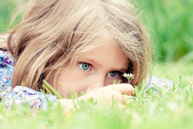 Kleines entzückendes Mädchen, das auf Gras liegt und Gänseblümchen betrachtet