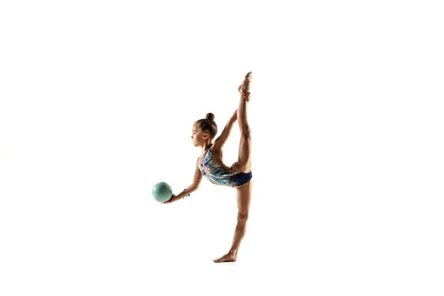 Kleines flexibles Mädchen lokalisiert auf weißer Wand. Kleines weibliches Modell als rhythmische Gymnastikkünstlerin im hellen Trikot. Anmut in Bewegung, Action und Sport. Übungen mit dem Ball machen.