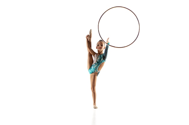 Kleines flexibles Mädchen lokalisiert auf weißer Wand. Kleines weibliches Modell als rhythmische Gymnastikkünstlerin im hellen Trikot. Anmut in Bewegung, Action und Sport. Übungen mit dem Reifen machen.