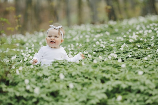 Kleines glückliches Mädchen sitzt unter den Blumen im Wald