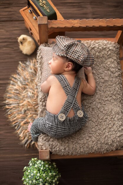 Kleines hübsches Baby des Neugeborenen, das auf Holzbett im Babyanzug und im Hut liegt