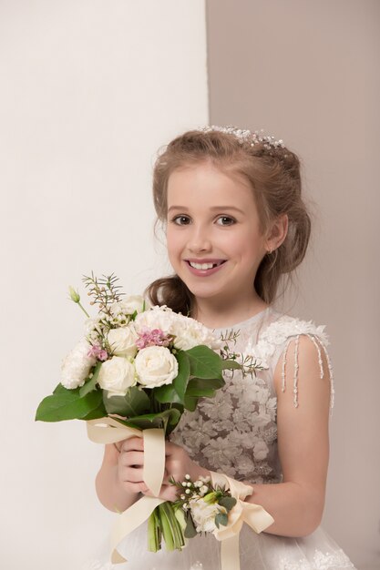 Kleines hübsches Mädchen mit Blumen in Brautkleidern gekleidet
