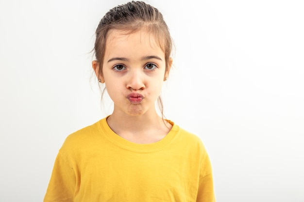 Kleines kaukasisches Mädchen macht lustige Gesichter auf weißem Hintergrund isoliert