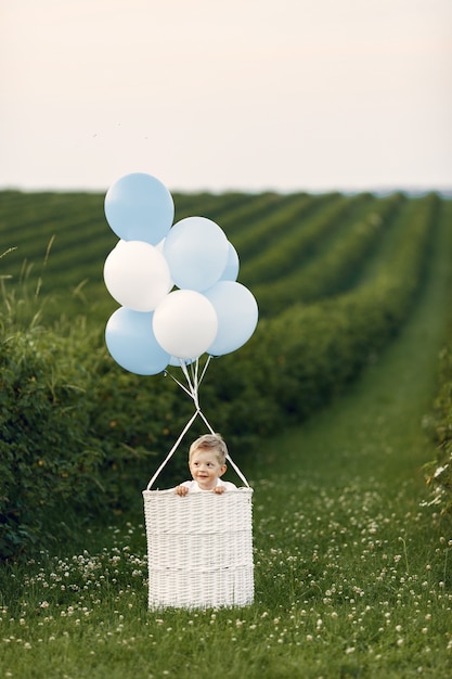 Kostenloses Foto kleines kind, das im korb mit luftballons sitzt
