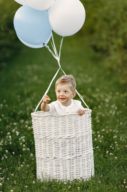 Kleines Kind, das im Korb mit Luftballons sitzt