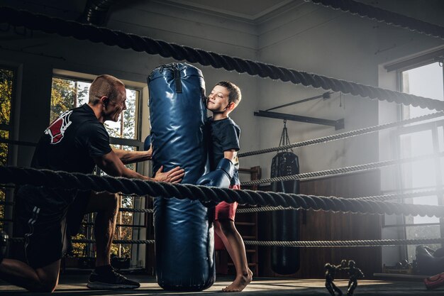 Kleines Kind hat ein ernsthaftes Boxtraining mit Trainer und Boxsack.