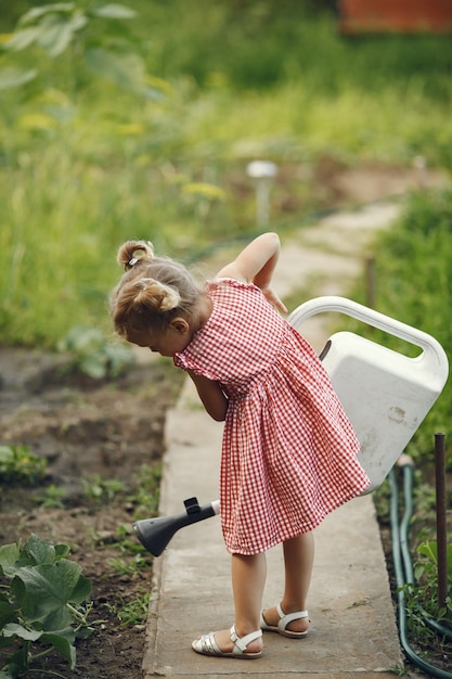 Kleines Kind mit einer Gießkanne mit Blumen gießen. Mädchen mit einem Trichter. Kind in einem rosa Kleid.