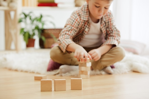 Kleines Kind sitzt auf dem Boden. Hübscher Junge, der mit Holzwürfeln zu Hause palying. Konzeptbild mit Kopie oder negativem Leerzeichen und Modell für Ihren Text