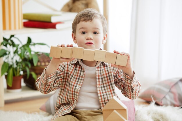 Kleines Kind sitzt auf dem Boden. Hübscher Junge, der zu Hause mit Holzwürfeln palying.