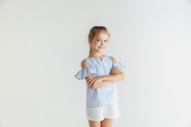 Kleines lächelndes Mädchen, das in der Freizeitkleidung auf weißem Studiohintergrund aufwirft