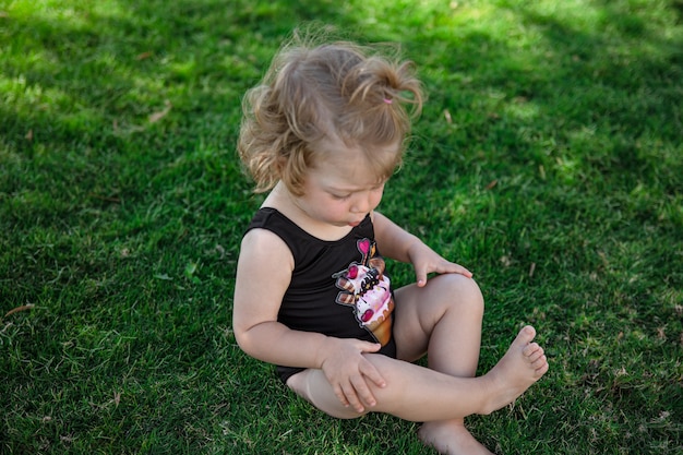 Kleines lustiges Mädchen im Sommer sitzt auf dem Gras im Garten