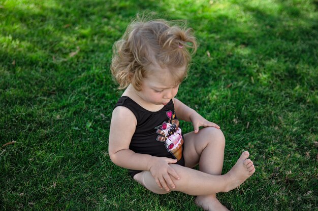 Kleines lustiges Mädchen im Sommer sitzt auf dem Gras im Garten