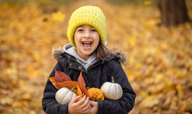 Kleines lustiges Mädchen mit Kürbissen im Herbstwald auf unscharfem Hintergrund