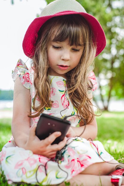 Kleines Mädchen auf dem Boden mit einem Smartphone sitzt