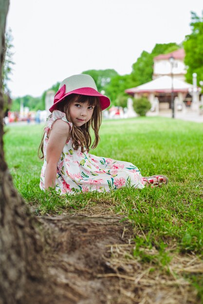 Kleines Mädchen auf dem Rasen eines Parks sitzen